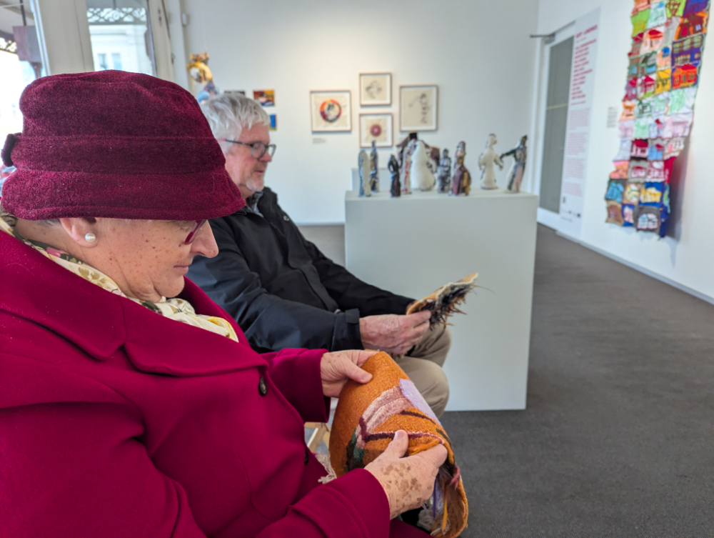 A man and woman each holding and inspecting a small piece of tapestry art