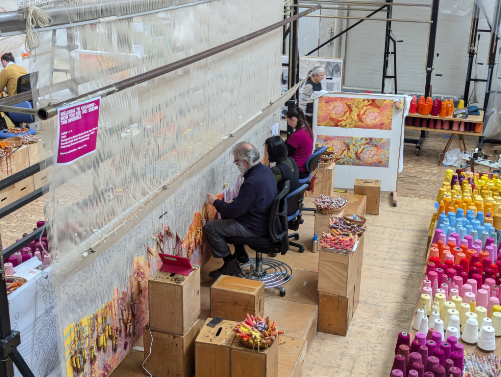 Four weavers sitting at a large loom at the Australian Tapestry Workshops